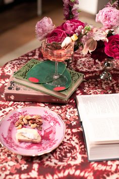 a pink plate topped with food next to a vase filled with flowers and a book