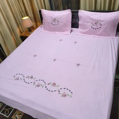 a bed with pink sheets and pillows on top of it next to a night stand