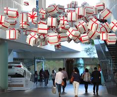 several people walking through a building with many wrapped presents hanging from the ceiling above them