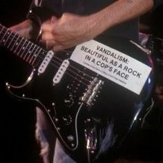 a man playing an electric guitar with a sign on it that says, vandalism beautiful as a rock in a cops face