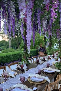 the table is set with plates and place settings under purple flowers hanging from the ceiling