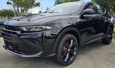 the front end of a black car parked in a lot with other cars behind it