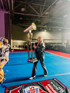 a woman holding a trophy while standing on top of a blue floor in front of an audience