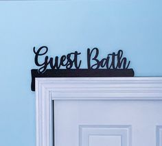 a metal sign that says guest bath on top of a white door with a blue wall in the background