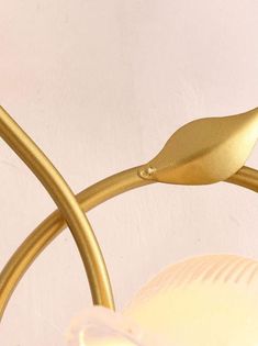 a close up of a light fixture with a gold leaf on the end and a white wall in the background