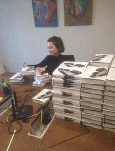 a woman sitting at a desk surrounded by stacks of books