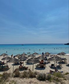 many umbrellas and chairs on the beach with people in the water behind them under a blue sky