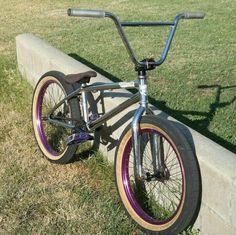 a bike parked on the side of a cement wall next to a grass field and sidewalk