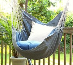 a blue hammock hanging from a wooden deck in the sun with pillows on it