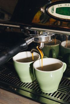 two green cups filled with coffee being poured into an espresso machine's drip