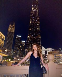 a woman standing on top of a bridge in front of a tall building at night