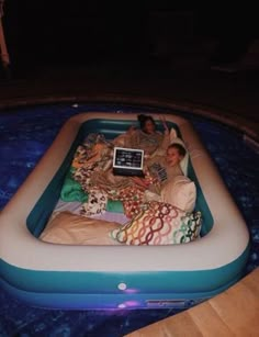 two people laying in an inflatable pool with a laptop on the back ground