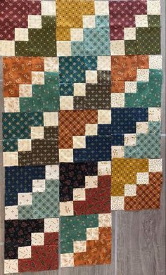 a quilt made with different colors and patterns on the side of a wooden table top