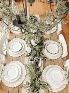 the table is set with white plates and silverware, greenery, and candlesticks