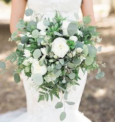 a bride holding a bouquet of white flowers and greenery in her hands on the ground