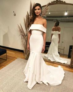 a woman is standing in front of a mirror wearing a white dress with an off the shoulder neckline