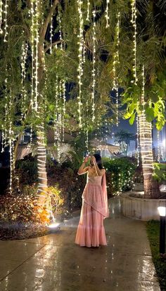 a woman is walking down the sidewalk in front of some trees with lights on them