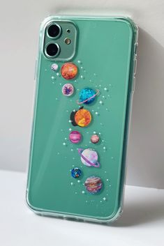 an iphone case with planets and stars painted on the back, sitting on a white surface