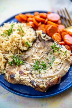 a blue plate topped with meat, rice and carrots next to a fork on a table