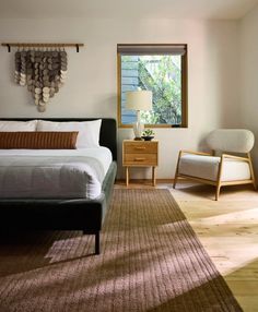 a bed sitting in a bedroom next to a chair and table with a lamp on top of it