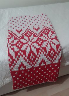 a red and white blanket sitting on top of a bed next to a wooden floor