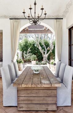 an outdoor dining area with a wooden table and chairs, chandelier and windows