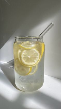 a glass filled with water and lemons on top of a white countertop next to a spoon