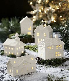 small white houses sitting on top of a wooden table next to a christmas tree with lights