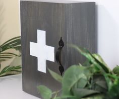 a wooden box with a white cross painted on the front and side, sitting next to a potted plant