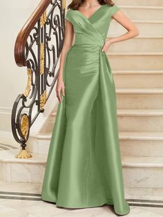 a woman in a long green dress standing next to a stair case with stairs and railings