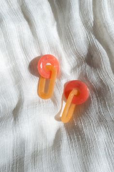 two orange and yellow ear clips laying on top of a white cloth covered bed sheet