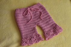 a pink crocheted baby pants laying on top of a yellow blanket