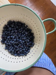 blueberries in a colander being held up by someone's hand on a wooden floor