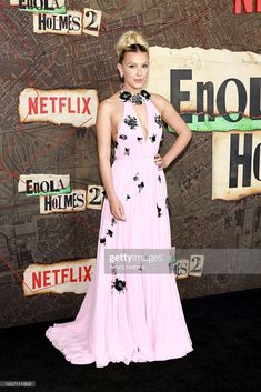 a woman in a pink dress poses on the red carpet at the end of an event