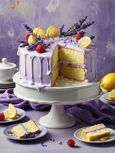 a white cake with purple icing and lemons on top, surrounded by plates