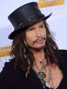 a man with long hair wearing a black top hat and necklaces on his neck