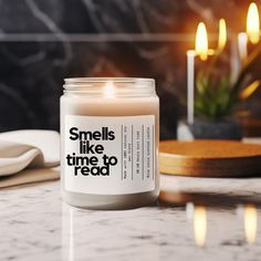 a candle that reads smells like time to read on the table next to some candles