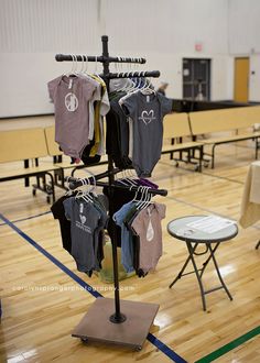 an indoor gym with tables, chairs and shirts on the clothes rack that is holding t - shirts