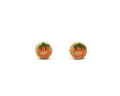 small orange pumpkin earrings with green leaves on the top and bottom, set against a white background