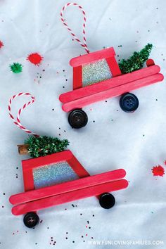 two red wooden toy cars decorated with glitter and christmas tree decorations on top of white paper