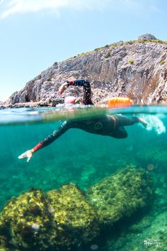 a person swimming in the water near rocks and corals with an orange life jacket on