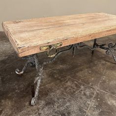 an old wooden table with wrought iron legs and wood planks on the top, sitting on a tile floor