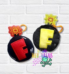 three different types of felt toys hanging on a brick wall, one with the letter f