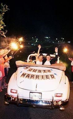 a couple riding in the back of a white car with sparklers on it's roof