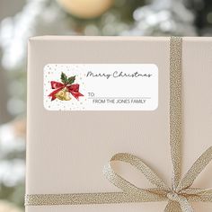 a gift box with a bow and merry christmas sticker on the front is sitting in front of a christmas tree