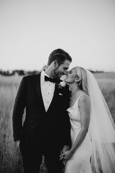 a bride and groom kissing in the middle of an open field with tall grass behind them