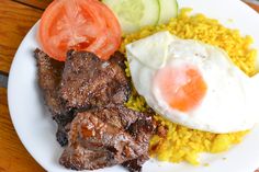 a white plate topped with meat, rice and veggies on top of a wooden table