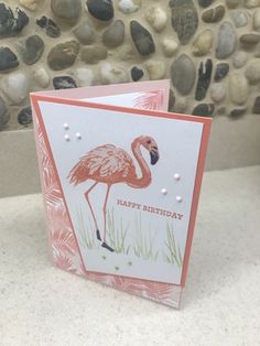 a pink flamingo birthday card on a table with rocks and pebbles in the background