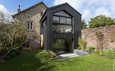 a black house sitting in the middle of a lush green field next to a stone building