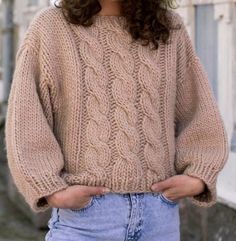 a woman standing in front of a building with her hands on her hips wearing a sweater